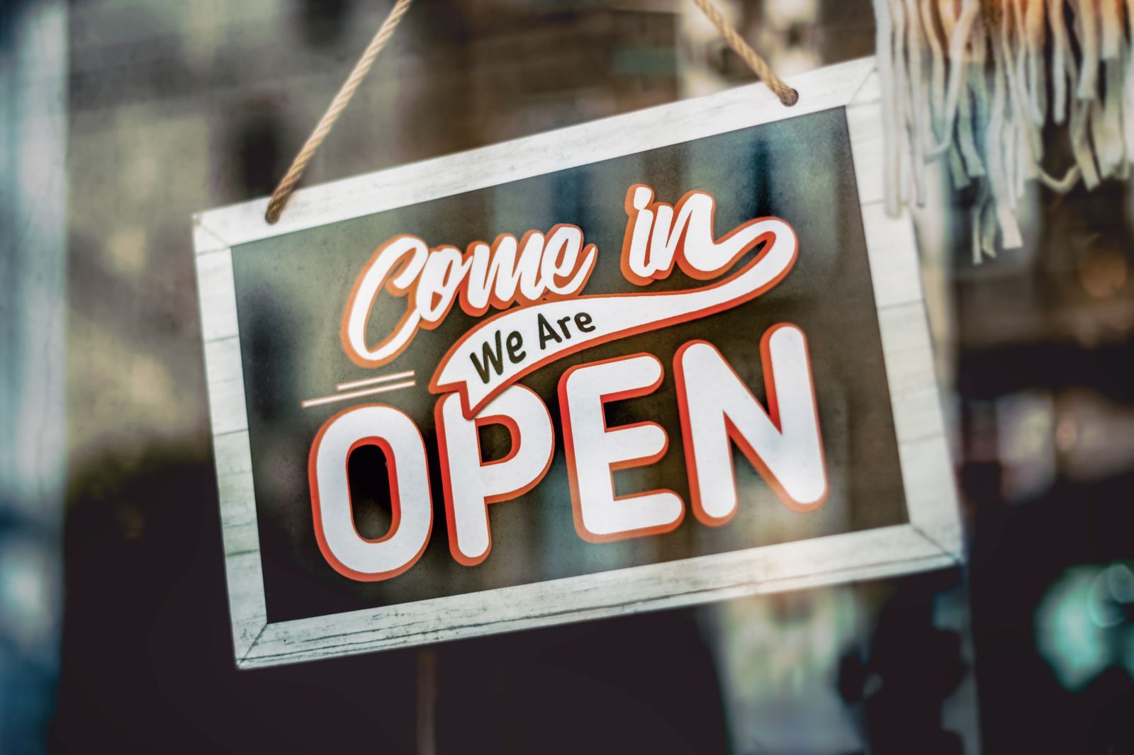 Hand-painted 'Come in, we're open' sign hanging in a shop window