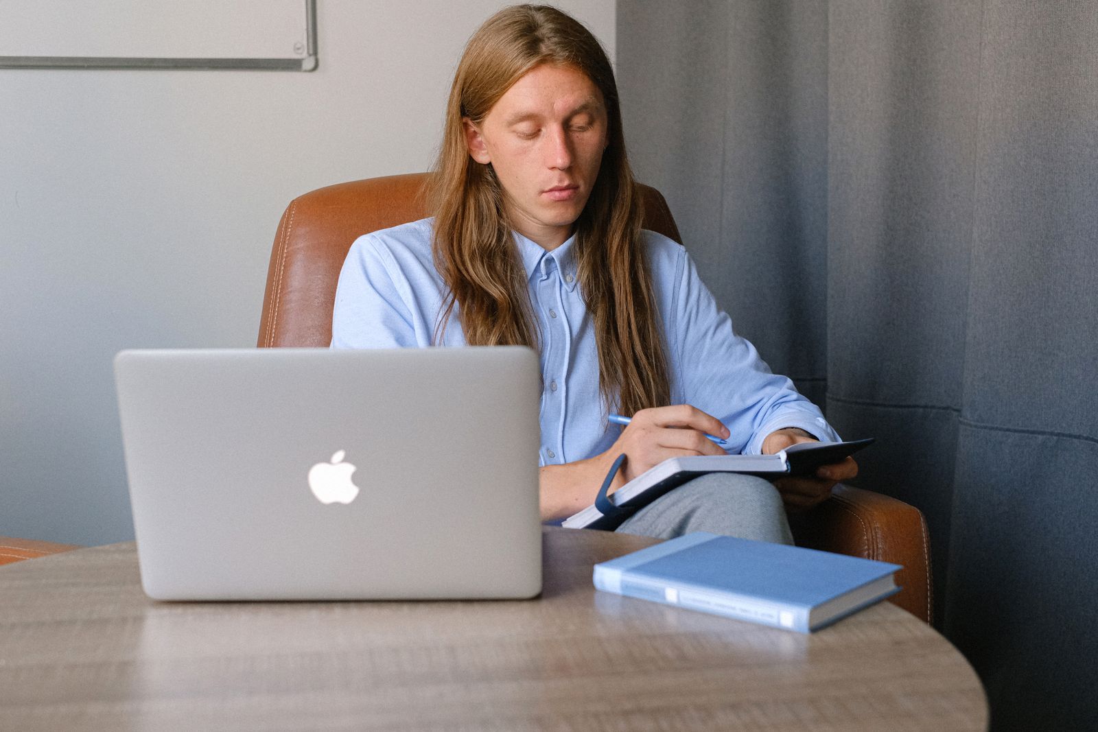 Man at a desk taking notes in a notebook while working on a laptop