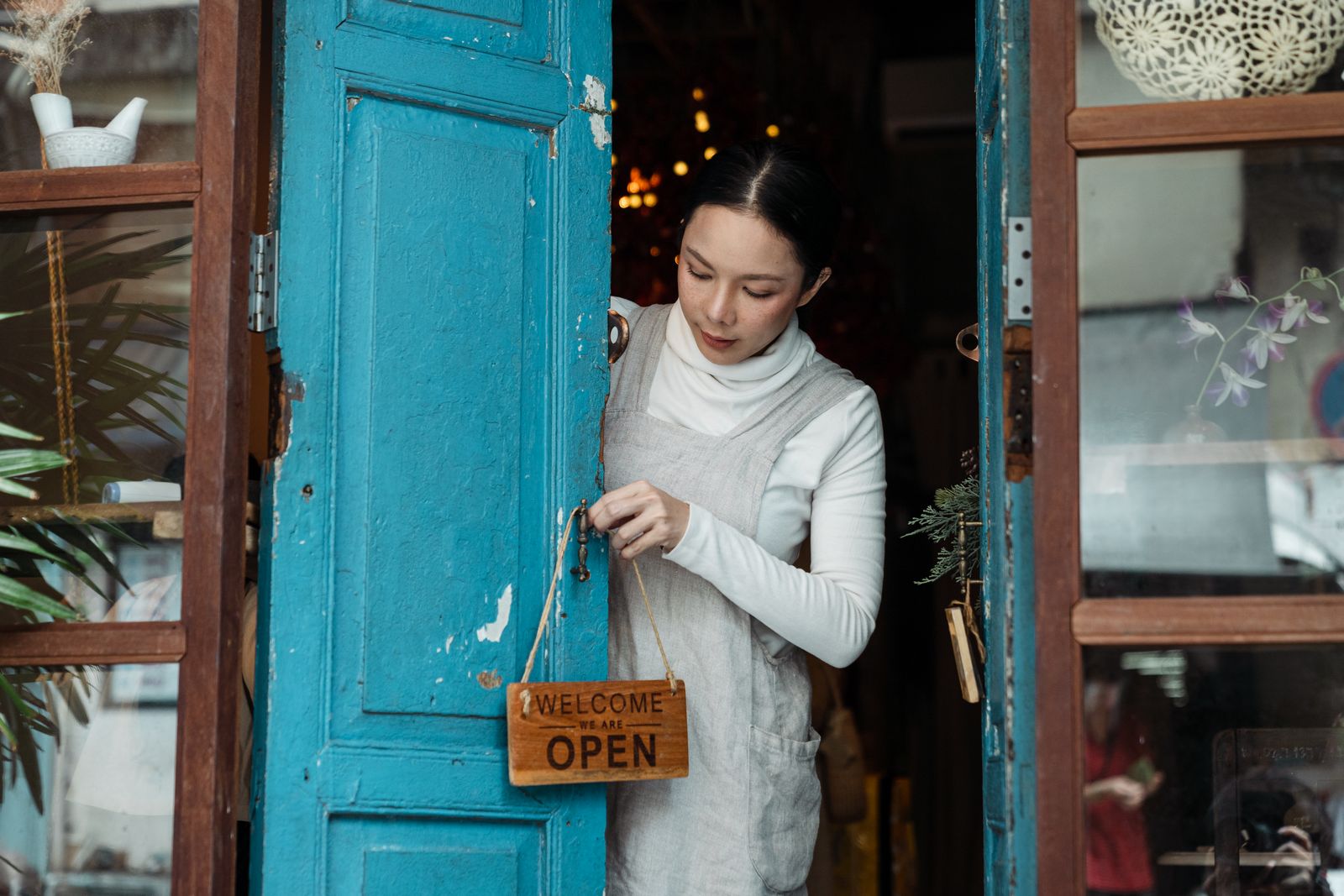 Café owner hanging an open sign on the blue wooden door of her shop