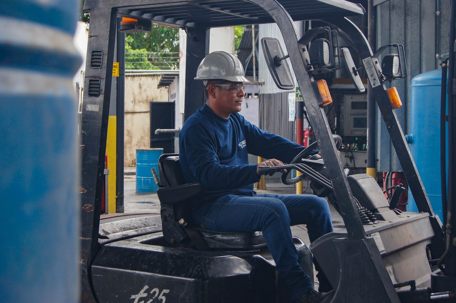 Warehouse worker in a hi-vis vest and helmet driving a forklift between racking